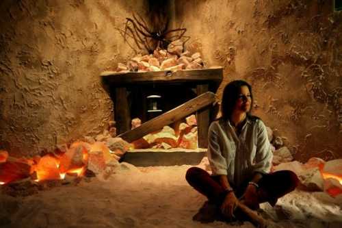 A person sits cross-legged in a cozy, salt-filled room with a stone fireplace and warm lighting.