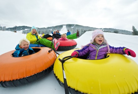 A group of children joyfully tubing down a snowy hill, wearing colorful winter gear and smiling in the winter landscape.