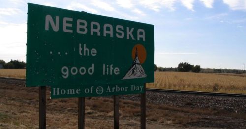 Sign for Nebraska, featuring the phrase "the good life" and "Home of Arbor Day," with a scenic background.