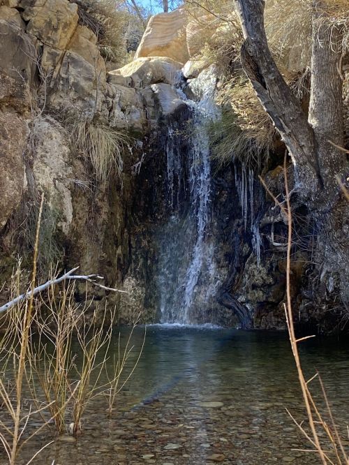 A serene waterfall cascades into a clear pool, surrounded by rocky terrain and sparse vegetation.