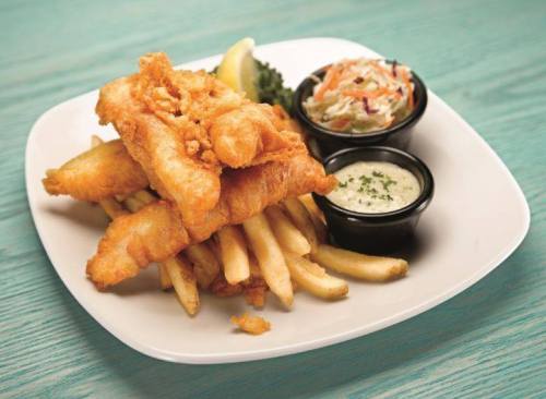 A plate of crispy fried fish fillets served with French fries, coleslaw, and dipping sauce, garnished with a lemon wedge.