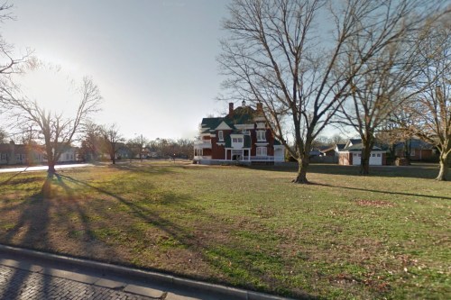 A large, historic house with a green roof, surrounded by bare trees and a grassy area, under a bright sky.