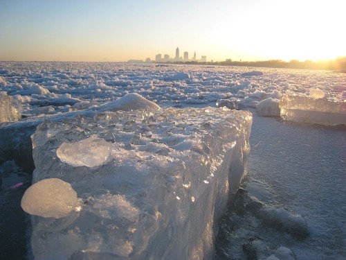 Ice formations on a lake with a city skyline in the background during sunset.