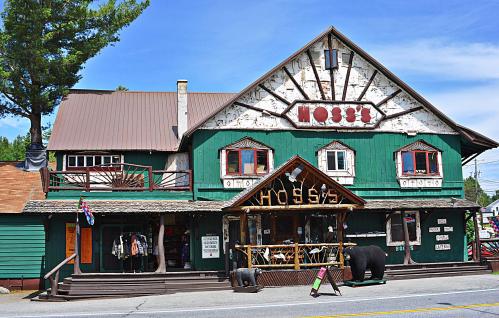 A rustic green building with a wooden porch, featuring a sign that reads "Hoss's" and decorative bear sculptures outside.