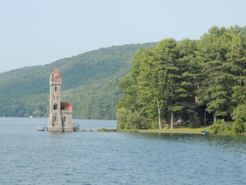 A scenic view of a lake with a tower on the shore, surrounded by lush green trees and rolling hills in the background.