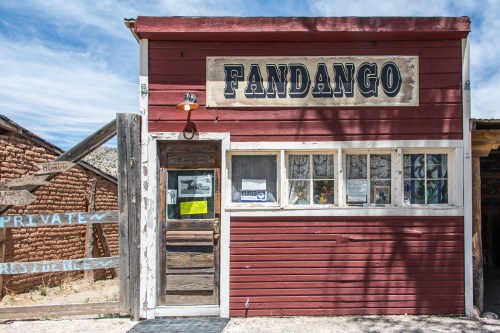 A rustic red building with a sign reading "Fandango," featuring a wooden door and nearby directional signs.