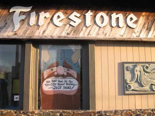 Sign on a building with "Firestone" above and a cartoon Viking below, promoting tire repair services.