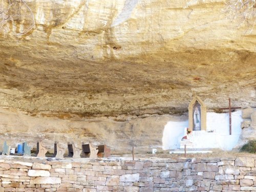 A cave with a small altar featuring a statue, surrounded by stone benches and a rocky overhang above.