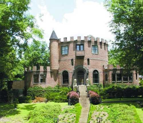 A brick castle-style house with a turret, surrounded by greenery and a well-maintained lawn.