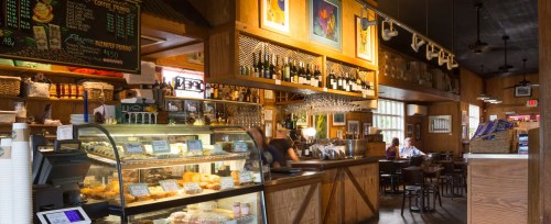 Cozy café interior with a display case of pastries, wooden decor, and patrons enjoying their meals at tables.