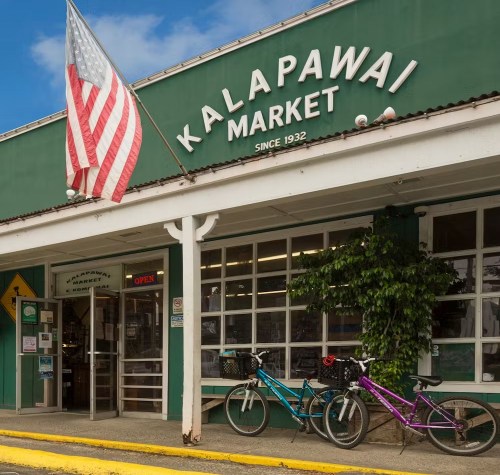 Exterior of Kalapawai Market, featuring an American flag, green facade, and two bicycles parked outside.