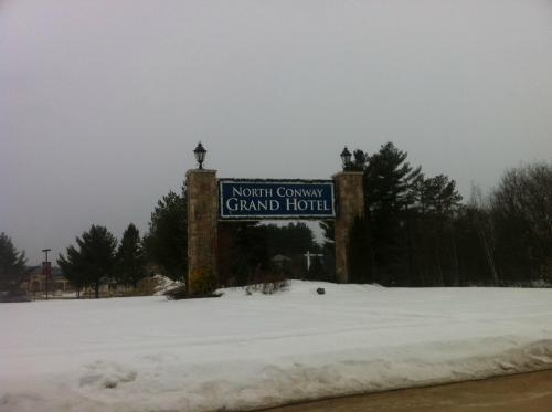 Sign for North Conway Grand Hotel, surrounded by snow and trees, on a cloudy day.