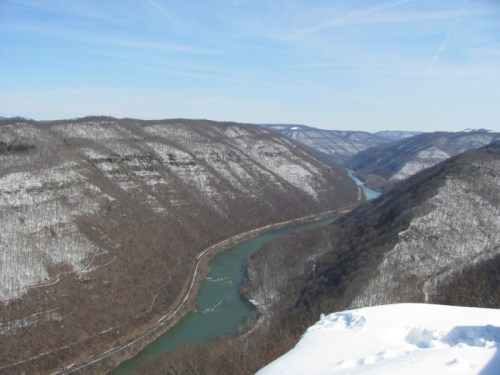 A scenic view of a winding river surrounded by snow-covered hills and trees under a clear blue sky.