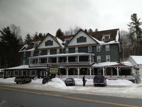 A large, historic hotel with a green exterior, surrounded by snow, and parked cars in front on a winter day.