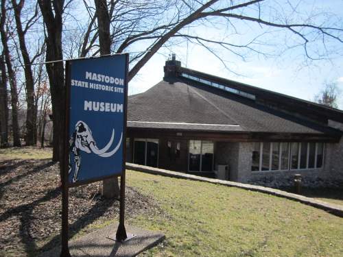 Sign for the Mastodon State Historic Site Museum in front of a modern building surrounded by trees.