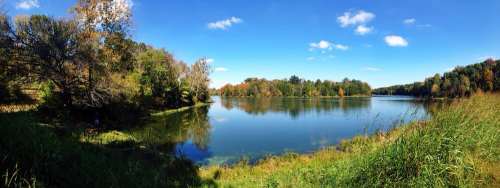A serene lake surrounded by colorful autumn trees under a clear blue sky. Reflections shimmer on the water's surface.