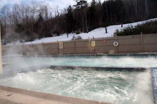 A steaming hot tub beside a snowy landscape, with trees and a fence in the background.