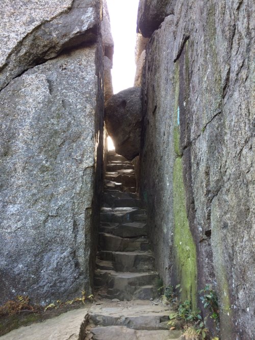 Narrow stone staircase between large rocks, leading upward into bright light.
