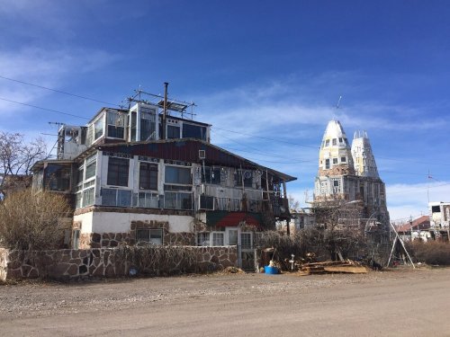 Abandoned buildings with unique architecture under a clear blue sky, surrounded by sparse vegetation.