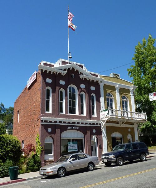 Historic buildings with a flag on top, featuring a mix of brick and stucco facades, parked cars in front.