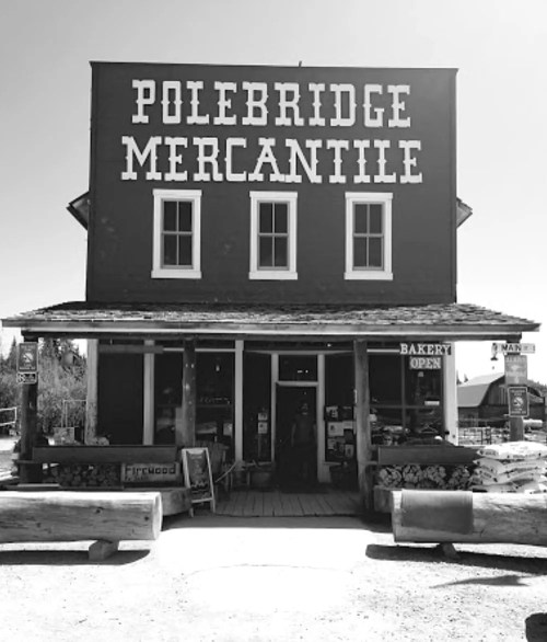 Black and white image of Polebridge Mercantile, a rustic store with a sign reading "Bakery Open" in front.