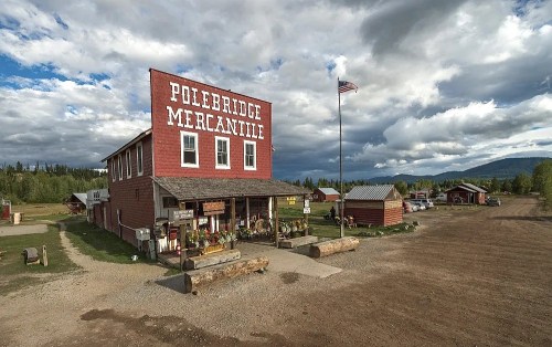 A rustic red mercantile building with "Polebridge Mercantile" sign, surrounded by trees and a cloudy sky.