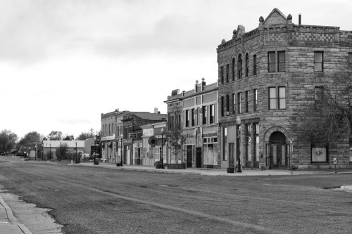 Black and white image of a quiet street lined with historic buildings and storefronts.