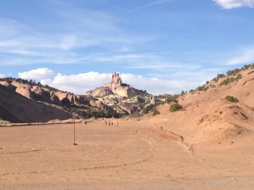 A vast desert landscape with rocky formations and a distant mountain under a blue sky, with a few people walking.
