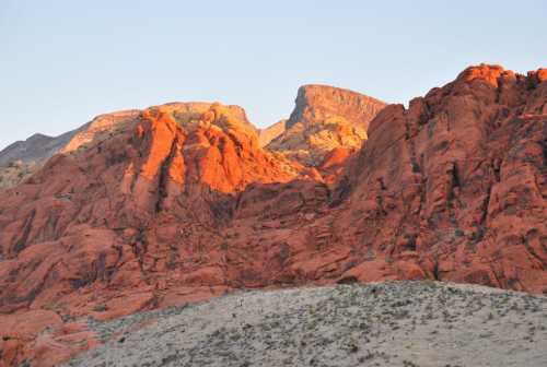 Sunset light illuminates red rock formations against a clear sky, highlighting the rugged landscape.