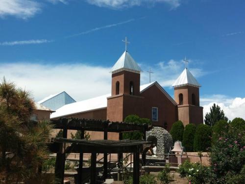 A church with two towers and crosses, surrounded by greenery and a blue sky with clouds.