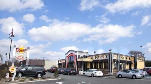 A diner with a bright yellow exterior and large windows, surrounded by parked cars under a partly cloudy sky.