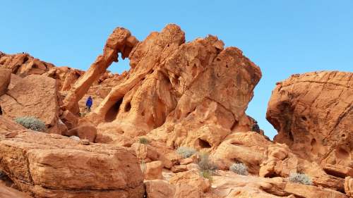 A person stands among large, reddish rock formations under a clear blue sky.