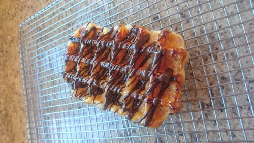 A freshly baked dessert on a cooling rack, drizzled with chocolate and caramel sauce.