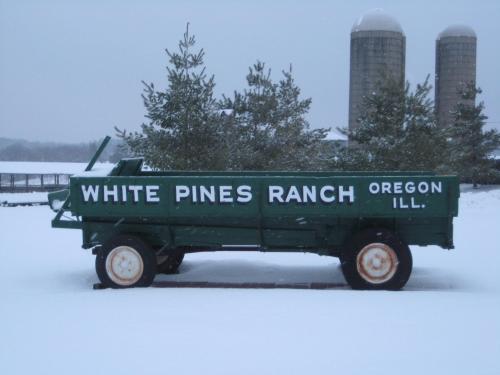 A green wagon labeled "White Pines Ranch" sits in the snow, with silos visible in the background.