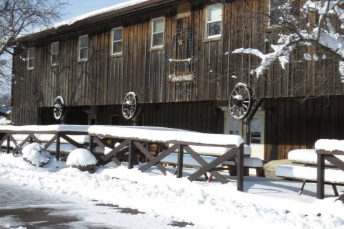 A rustic wooden building with a sign reading "Ranch House," surrounded by snow and featuring wagon wheels on the fence.