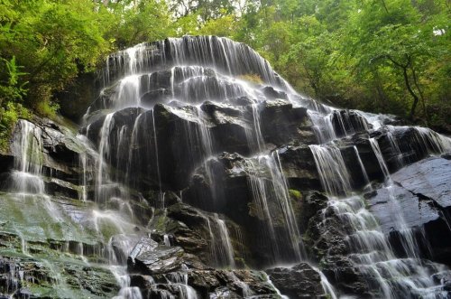 A cascading waterfall flows over dark rocks, surrounded by lush green foliage.
