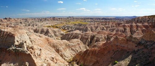 A panoramic view of rugged, colorful badlands with layered rock formations under a clear blue sky.
