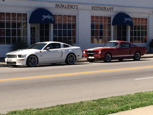 Two cars parked on a street in front of Papaleno's Restaurant: a white modern Mustang and a red classic Mustang.