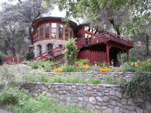 A unique round stone house with a wooden deck, surrounded by lush greenery and colorful flowers.