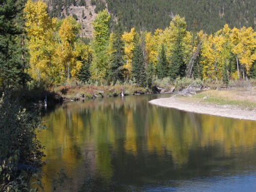 A serene river surrounded by vibrant autumn trees reflecting in the water, set against a mountainous backdrop.