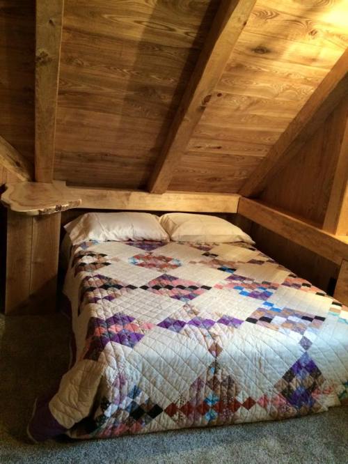 Cozy attic bedroom with a wooden ceiling, featuring a double bed covered in a colorful quilt.
