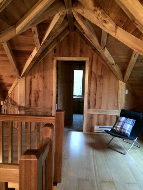 Interior of a wooden cabin with exposed beams, a doorway leading to another room, and a chair in the corner.
