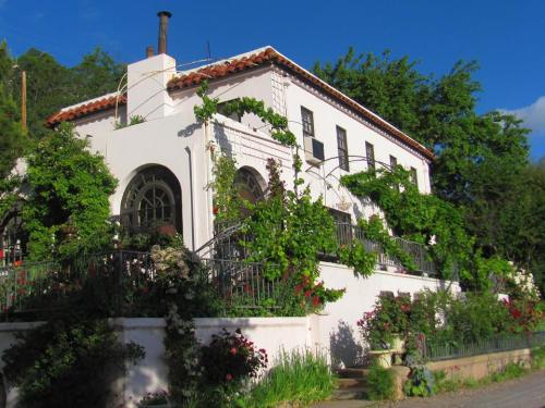 A charming white house with a red-tiled roof, surrounded by lush greenery and colorful flowers under a blue sky.