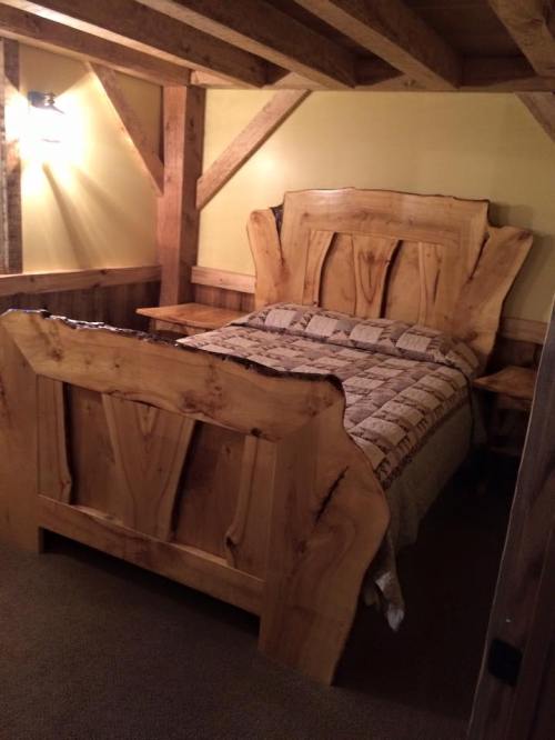 A rustic wooden bed with a unique headboard and matching side tables in a cozy, warmly lit room.