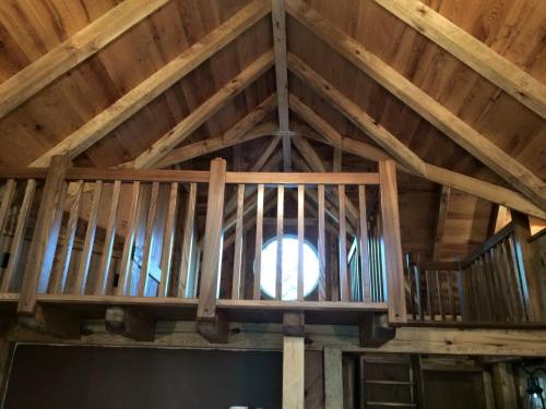 Interior view of a wooden loft with a circular window and exposed beams, showcasing rustic architecture.