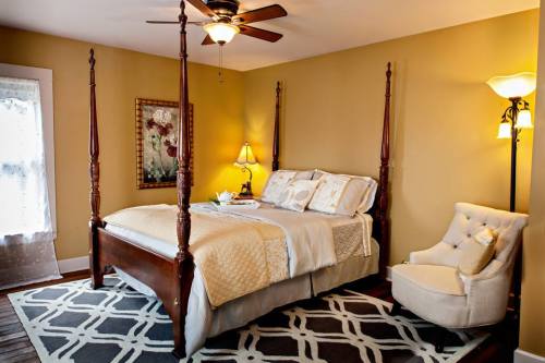 Cozy bedroom with a four-poster bed, soft lighting, and a comfortable armchair, featuring warm yellow walls.