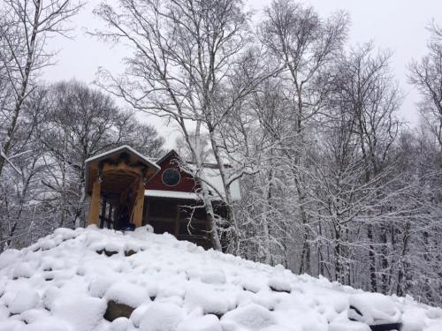 A cozy cabin surrounded by snow-covered trees and a rocky landscape in a winter setting.
