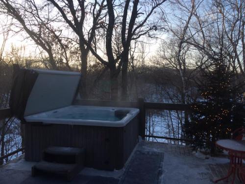A hot tub on a deck surrounded by trees, with a snowy landscape and a decorated tree in the background at sunset.