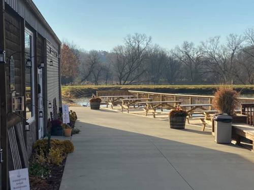 A serene riverside view with picnic tables, planters, and a pathway beside a building on a clear day.