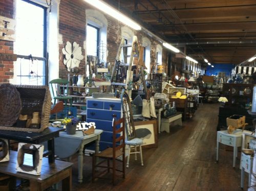 A spacious vintage shop filled with various furniture, decor items, and wooden displays under bright lighting.